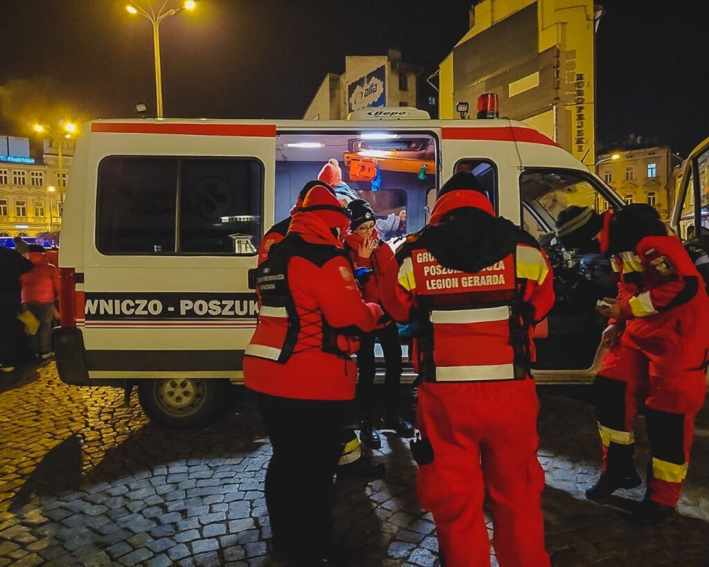 Pomoc na granicy: ratownicy w czerwonych kurtkach przy otwartym ambulansie nocą