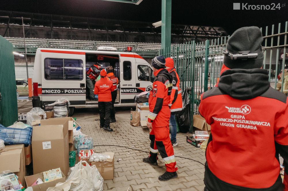 Ratownicy przy ambulansie i kartonach z darami nocą w punkcie pomocy